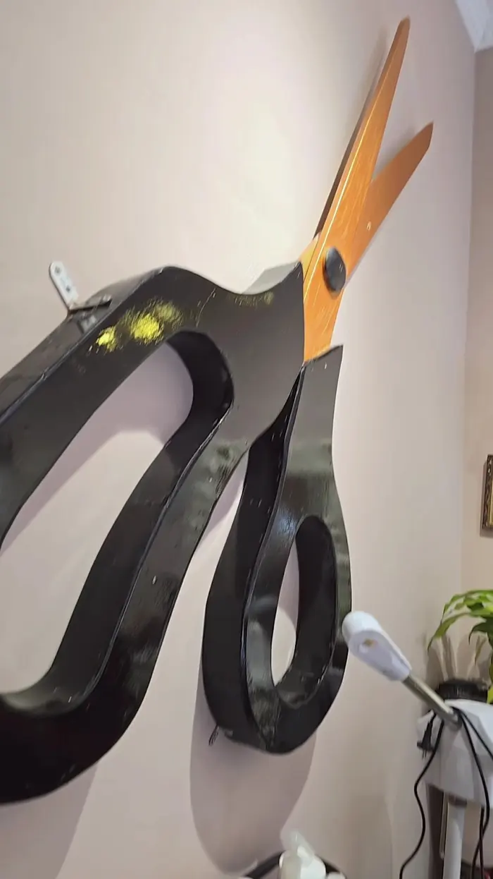 Close view of the giant black-handled scissors with copper blades mounted on the salon wall
