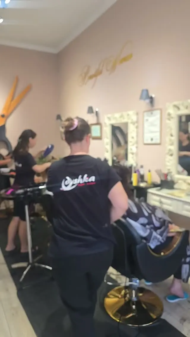 A stylist seen from behind in a black shirt with the Dyshka logo, working at the mirrors